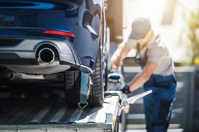 Man ties down a blue car on a tow truck